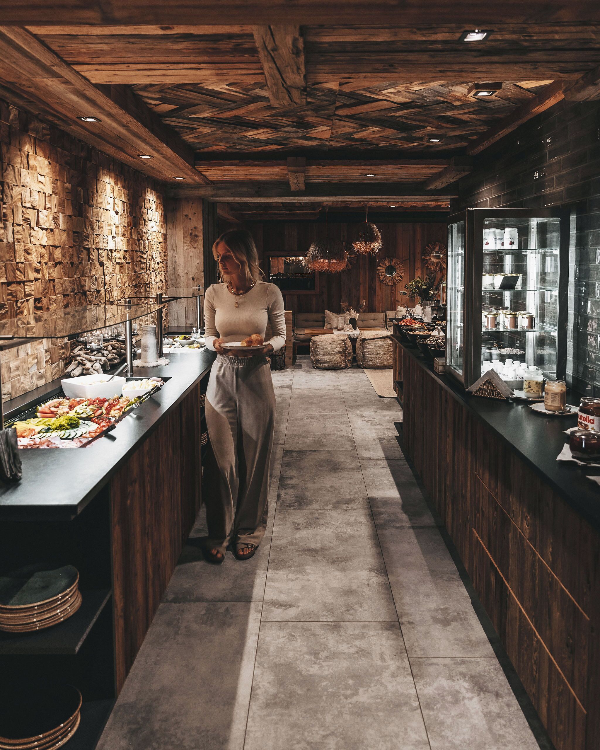 Eine Frau in einem Restaurant mit Holzeinrichtung, einem Buffet mit verschiedenen Speisen und einem Kühlschrank mit Getränken.