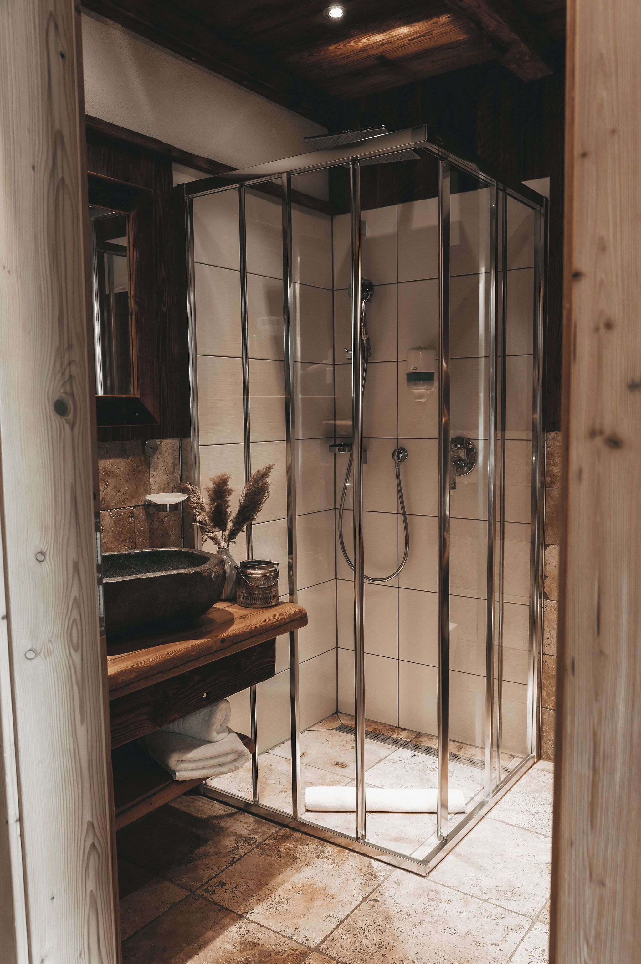 Una ducha con puertas de vidrio, un estante de madera con toallas y un revestimiento de azulejos.