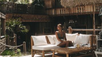 Une terrasse en bois avec un jacuzzi, une chaise longue et une structure dotée d’un toit de chaume.