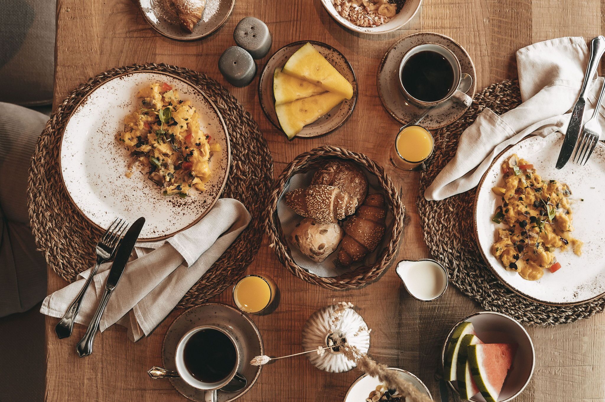 Ein gedeckter Frühstückstisch mit Speisen, Brot und Getränken auf einer Holztischplatte.