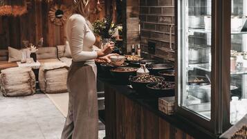 Una mujer de pie frente a una barra con distintos alimentos, en una habitación con paredes de madera y un salpicadero de ladrillo.