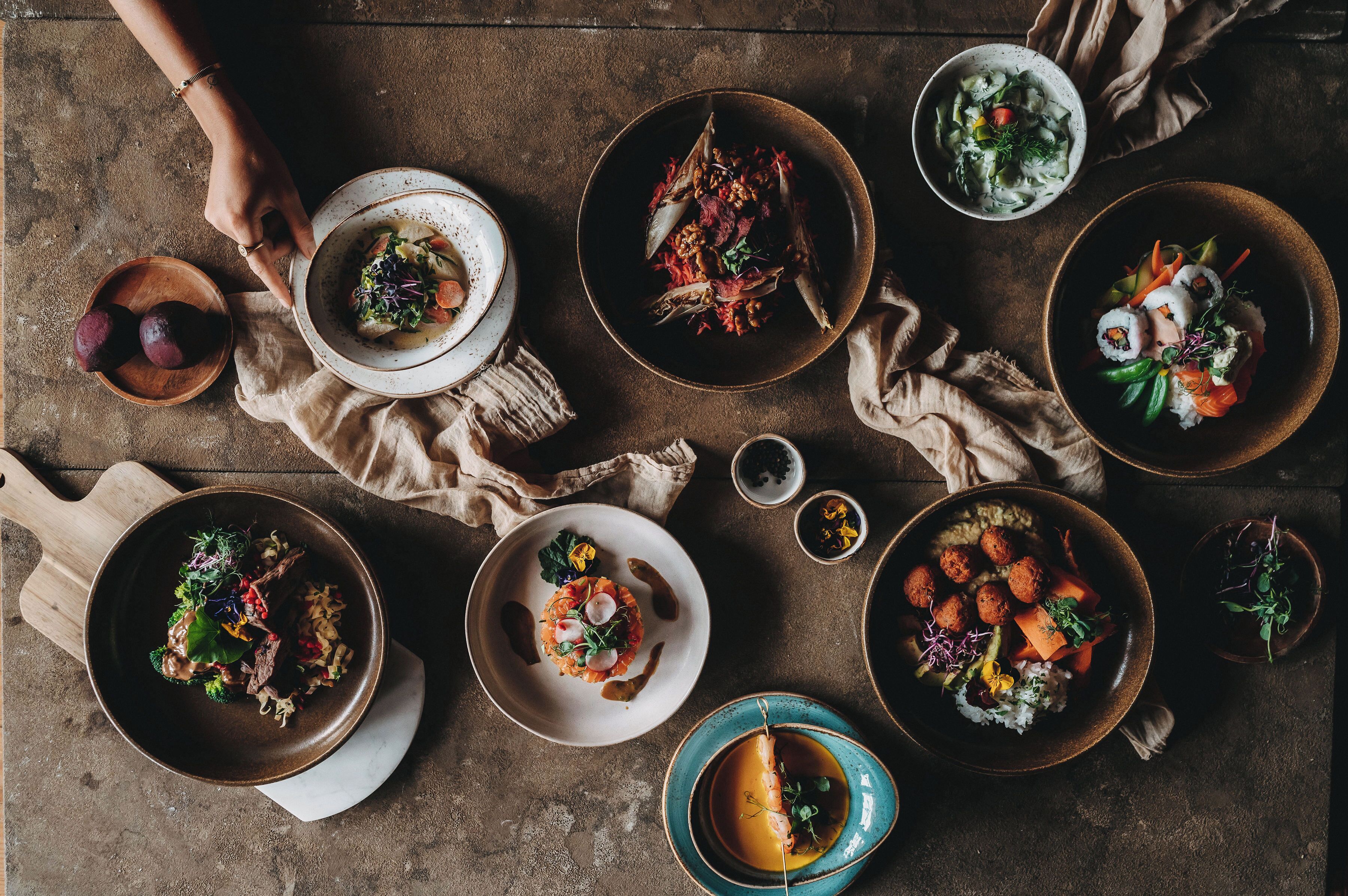 A top-down view of a dining table with various dishes, including sushi and salads, on a rustic wooden table.