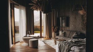 Ein modernes Schlafzimmer mit einem großen Bett, einer Couch, einem Couchtisch und Blick auf einen Garten durch das Fenster.