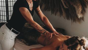 Sesión de terapia de masaje en una habitación con una cama, una decoración grande de plumas y una ventana con diseño de cuadrícula.