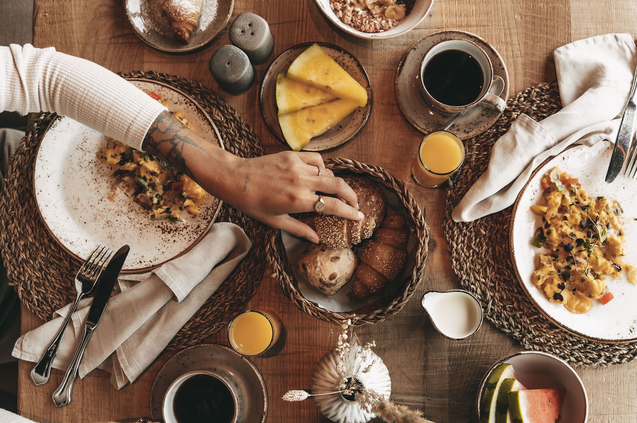 Une table dressée pour le petit-déjeuner, avec différents plats, notamment des toasts, des œufs brouillés et des fruits.