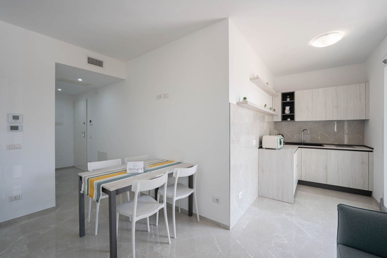 A modern kitchen with white cabinetry, a dining area with a table and chairs, and a visible door leading to another room.