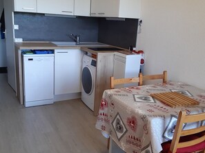 A compact kitchen with a washing machine, a small refrigerator, and a table with a patterned tablecloth. - Cozy Studio-Mezzanine for 4 with Balcony, Ski Locker, and Parking in Crest-Voland (Crest-Voland)