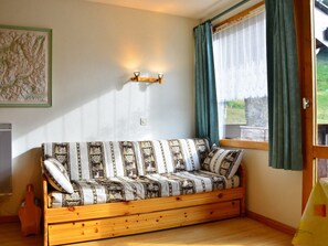 A cozy room with a wooden sofa, a map on the wall, and a window with curtains.