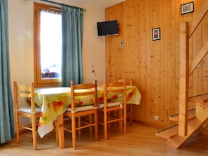 A wooden-paneled room with a dining table and chairs, a TV mounted on the wall, and a staircase. - Ski-In/Ski-Out Duplex, Sleeps 7, Balcony, Renovated, 1 Min to Shops, Free Parking, No Pets (La Plagne Montchavin Les Coches)
