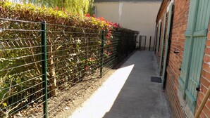 A narrow alleyway with a metal fence on one side and a brick wall on the other. - Charming Cottage in Tranquil Village with Private Parking and Baby Equipment (Villemurlin)