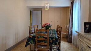 A dining area with a wooden table and chairs, a vase of flowers, and a television on a cabinet. - Charming Cottage in Tranquil Village with Private Parking and Baby Equipment (Villemurlin)