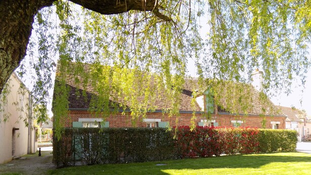 A brick building with a tiled roof, surrounded by a well-maintained lawn and a hedge. - Charming Cottage in Tranquil Village with Private Parking and Baby Equipment (Villemurlin)