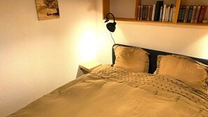 A bedroom with a bed, a nightstand, a lamp, a bookshelf, and a painting on the wall. - Cozy 4-Person Apartment, 200m from Slopes and Shops, South-West Balcony (Crest-Voland)
