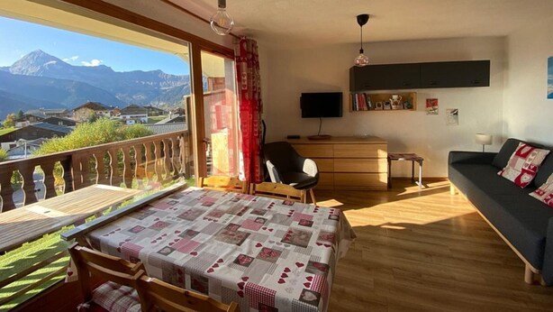 A bedroom with a bed, a desk, a chair, a sofa, and a balcony with a view of mountains. - Cozy 4-Person Apartment, 200m from Slopes and Shops, South-West Balcony (Crest-Voland)