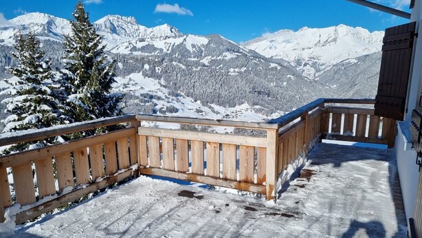 Un balcón de madera con vistas a montañas nevadas.