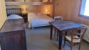 Habitación de madera con cama, una mesa y sillas. Tiene una ventana y un radiador.