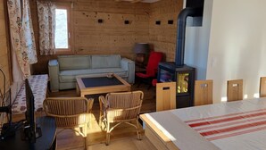 Una habitación acogedora con un sofá, dos sillones, una mesa, una silla roja, una lámpara y una estufa de leña.