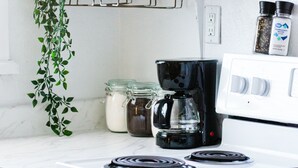 A kitchen with a white stove, black coffee maker, and various kitchen items on shelves. - Your dog gets a private fenced yard. You get a quiet East Hill home base minutes from downtown, the beach, and everything you came to Pensacola to enjoy. (Pensacola)