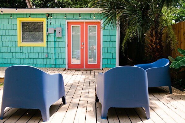 A house with a turquoise exterior, a red door, and a wooden deck with two blue chairs. - Your dog gets a fenced yard. You get a quiet East Hill home base minutes from downtown, the beach, and everything you came to Pensacola to enjoy. (Pensacola)