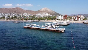 A waterfront area with a docked boat, a pier with umbrellas, and buildings in the background. - SUNDANCE SUITES HOTEL (Bodrum)