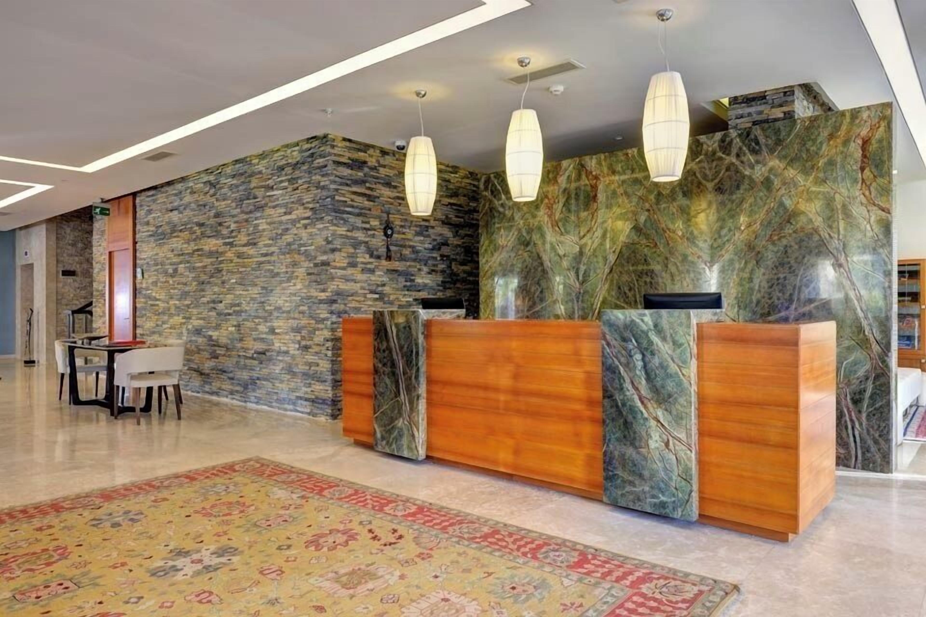 Una zona de recepción con pared de piedra, mostrador de madera y alfombra estampada.