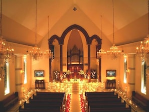 An interior with a central aisle, pews, chandeliers, and a large organ.