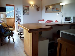 Ein gemütlicher Raum mit Holztisch, Stuhl, Bett mit roten Kissen und einem aufgehängten Hirschkopf.
