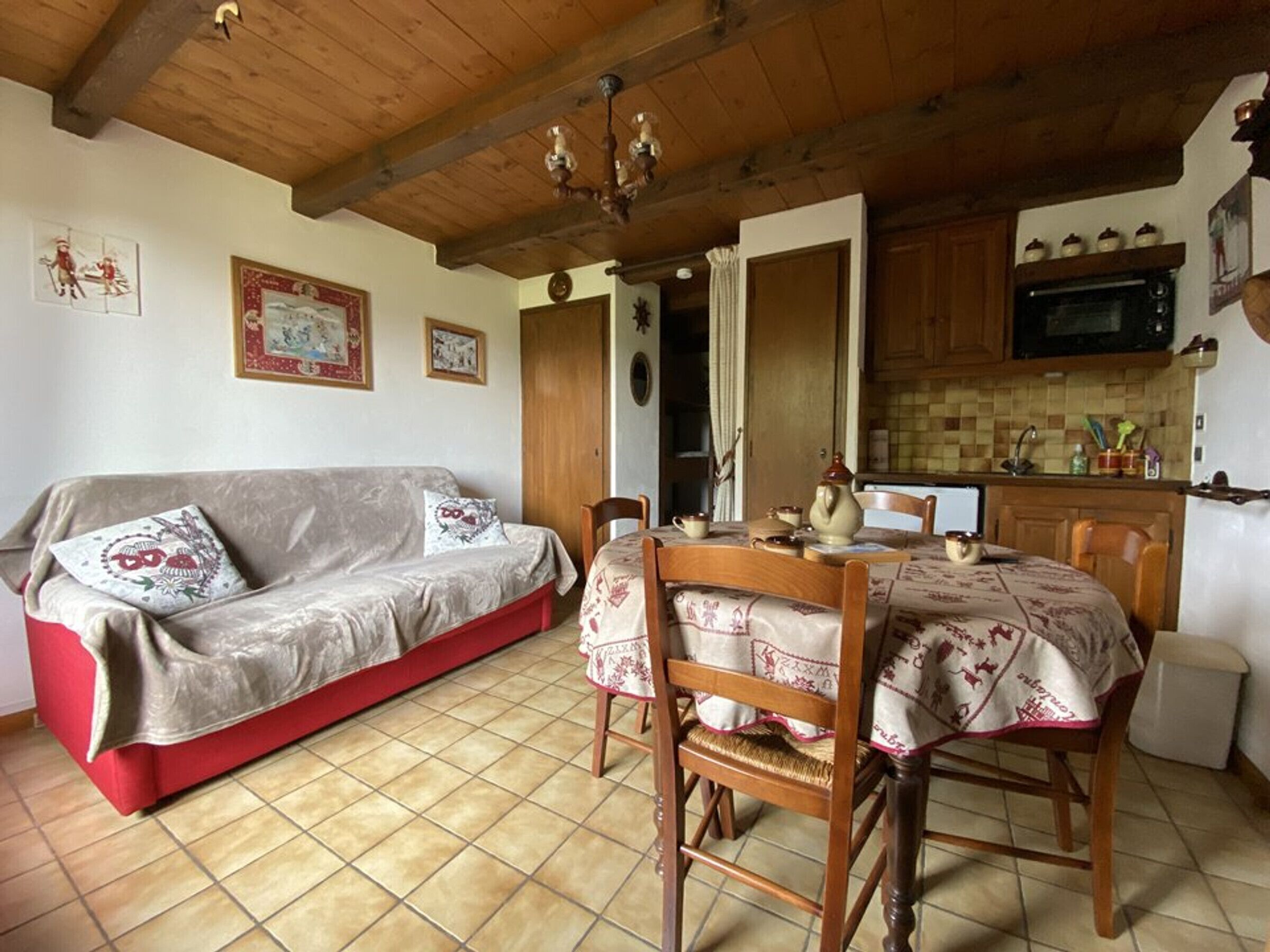 Ein gemütliches Wohnzimmer mit einem roten Sofa, einem Holzespeisetisch mit Stühlen und einer Küchenzeile inklusive Schränken und Mikrowelle.
