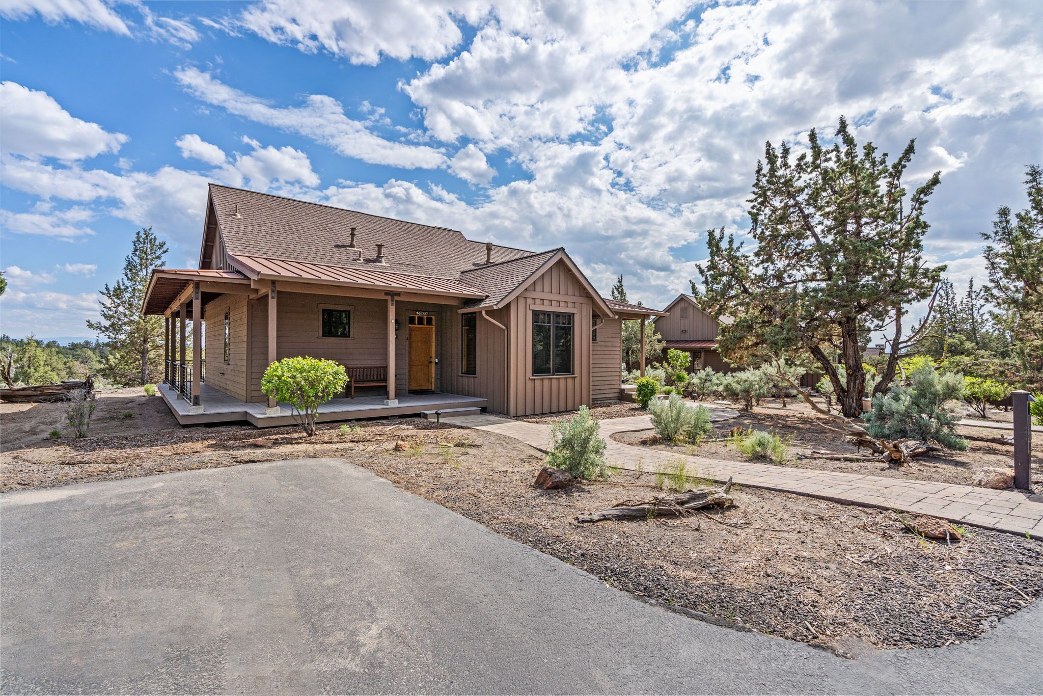 A single-story house with a front porch, a driveway, and a landscaped garden with various shrubs and trees.