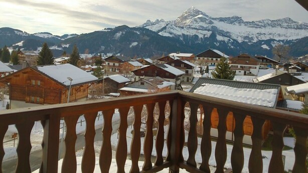 Un balcón de madera con vistas a un pueblo cubierto de nieve y una montaña al fondo.