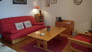 Una sala de estar acogedora con un sofá rojo, una mesa de centro de madera y un pequeño armario de madera.