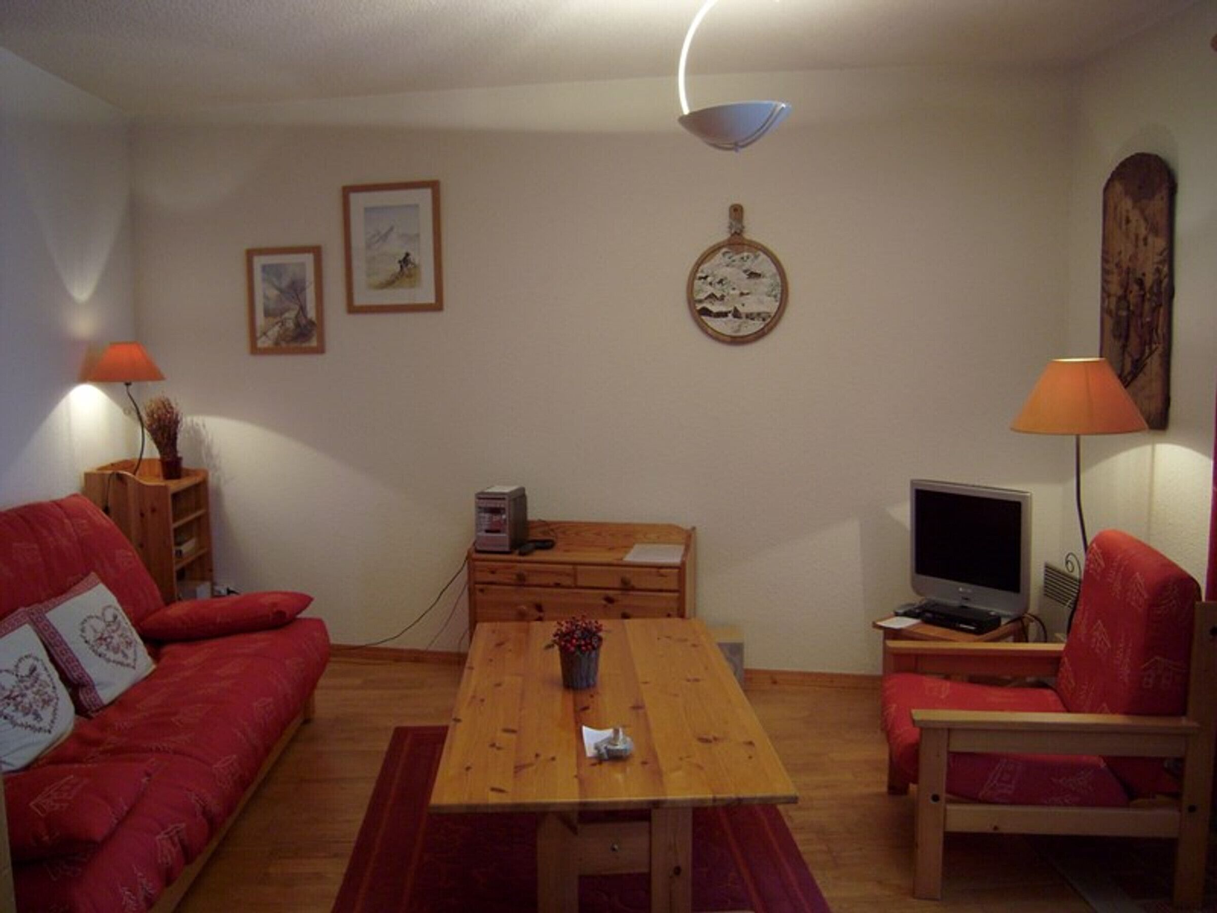 A cozy living room with a red sofa, a wooden coffee table, a TV, and a lamp.