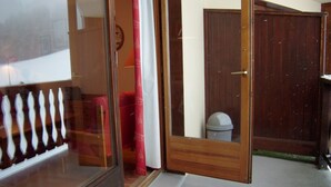 Una puerta de madera con un panel de vidrio, una cortina roja y una pared blanca con un reloj.