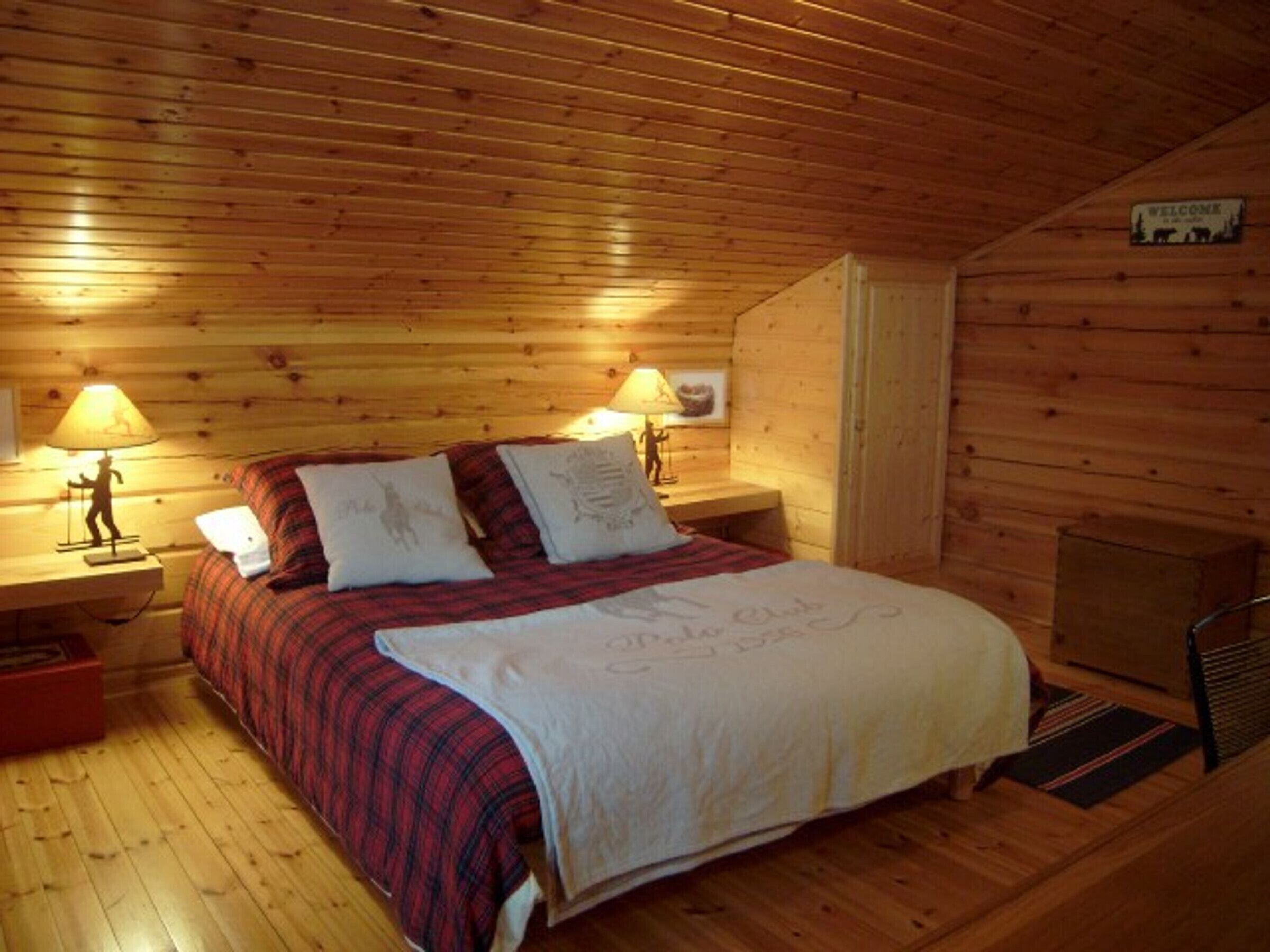 Una habitación acogedora tipo cabaña de madera con una cama, dos lámparas de noche y un cartel de bienvenida.