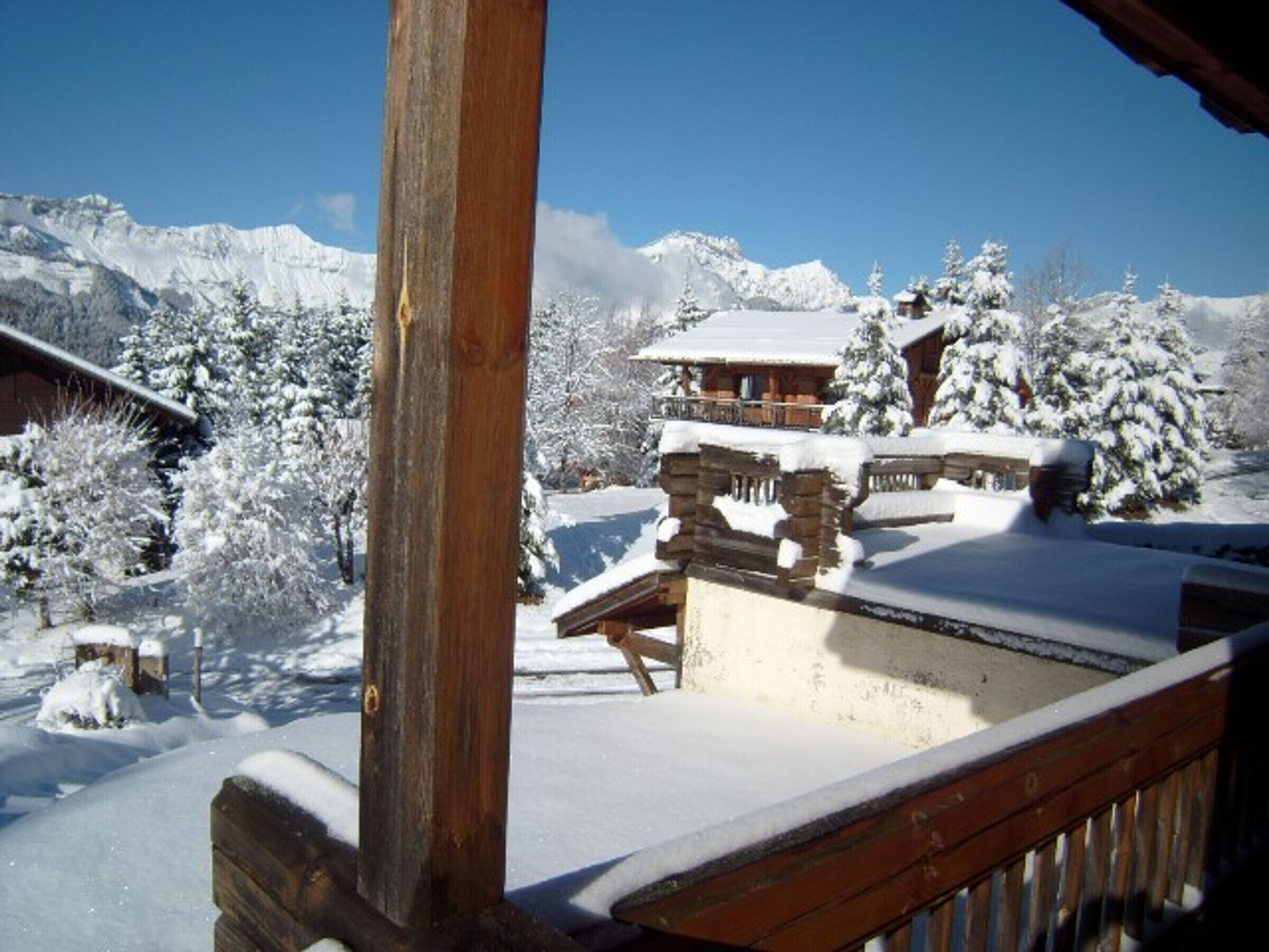 A wooden cabin with a snow-covered deck and a mountain backdrop.