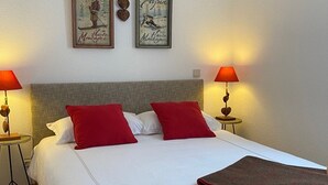 Una cama bien hecha con ropa de cama blanca y roja, dos lámparas de noche y dos cuadros en la pared.