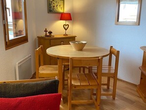 A dining area with a round wooden table, four wooden chairs, a small wooden side table with a lamp, and a bowl on the table.