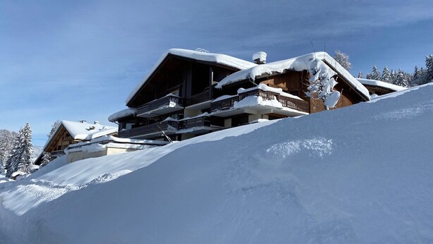 Una cabaña de madera con balcón, rodeada de árboles cubiertos de nieve.