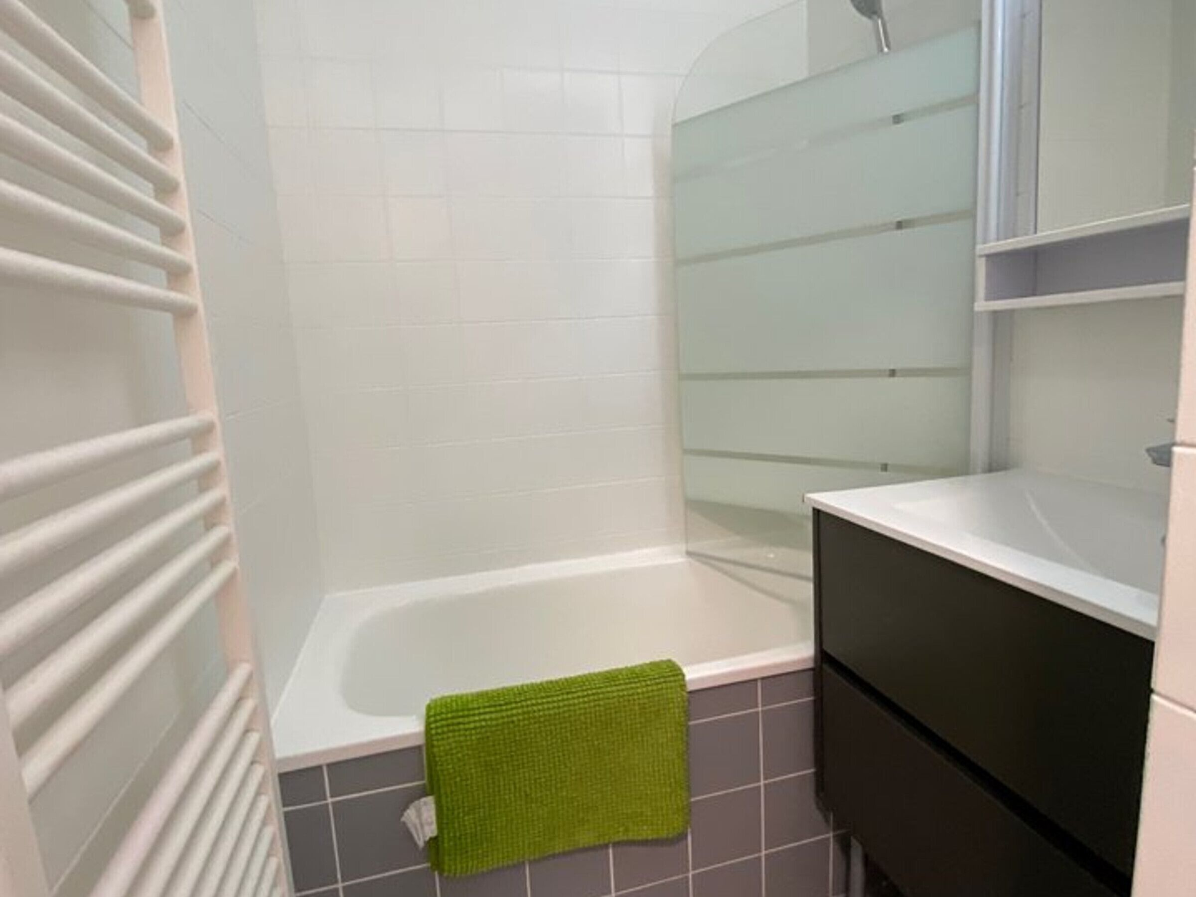 A bathroom with a bathtub, a green towel, and a white sink.