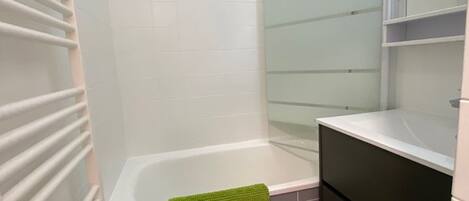 A bathroom with a bathtub, a green towel, and a white sink.