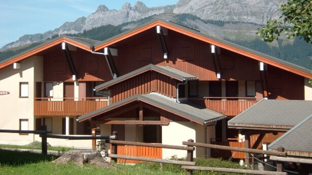 Et chalet-lignende hus med skråt tag, træfacade og mange vinduer.