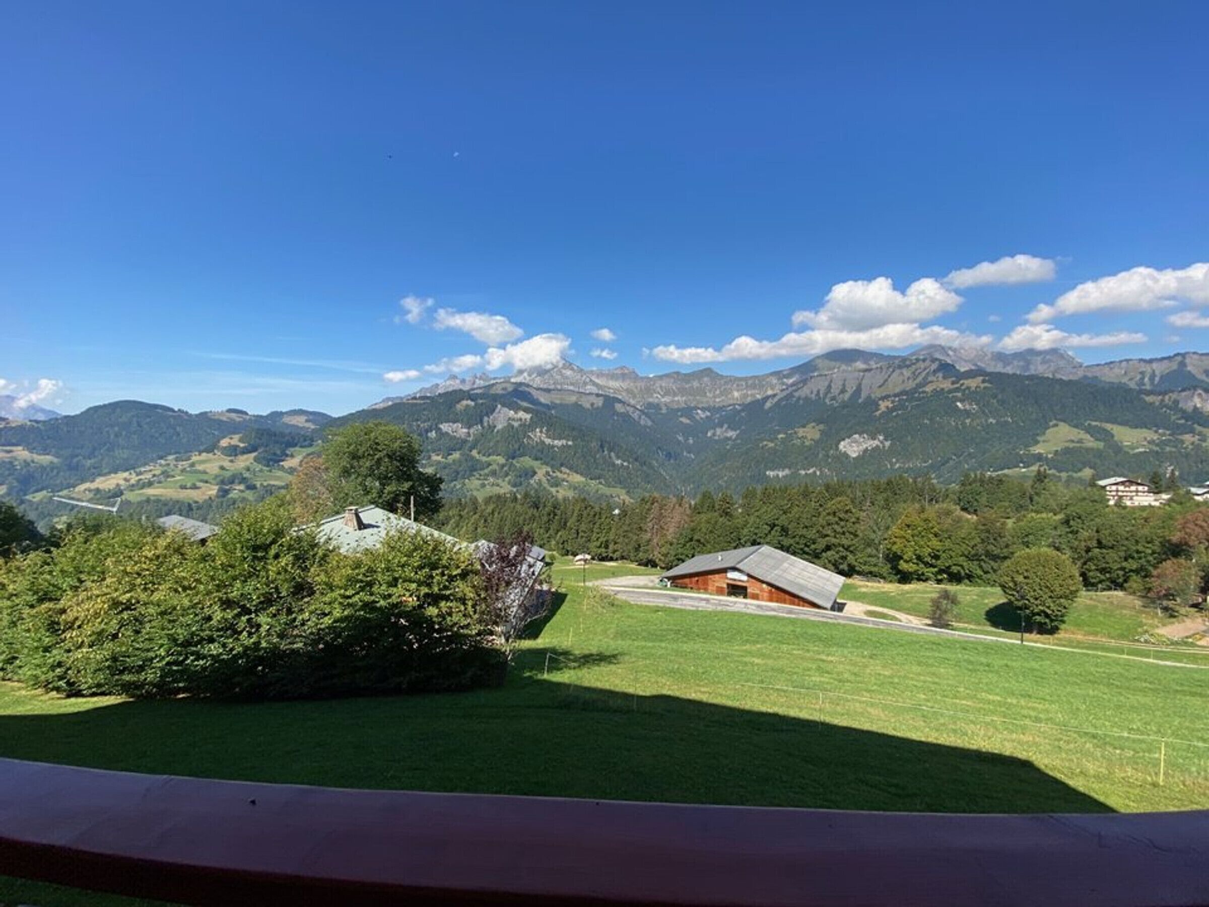 Paisagem montanhosa com céu claro, um campo gramado e uma cabana de madeira.