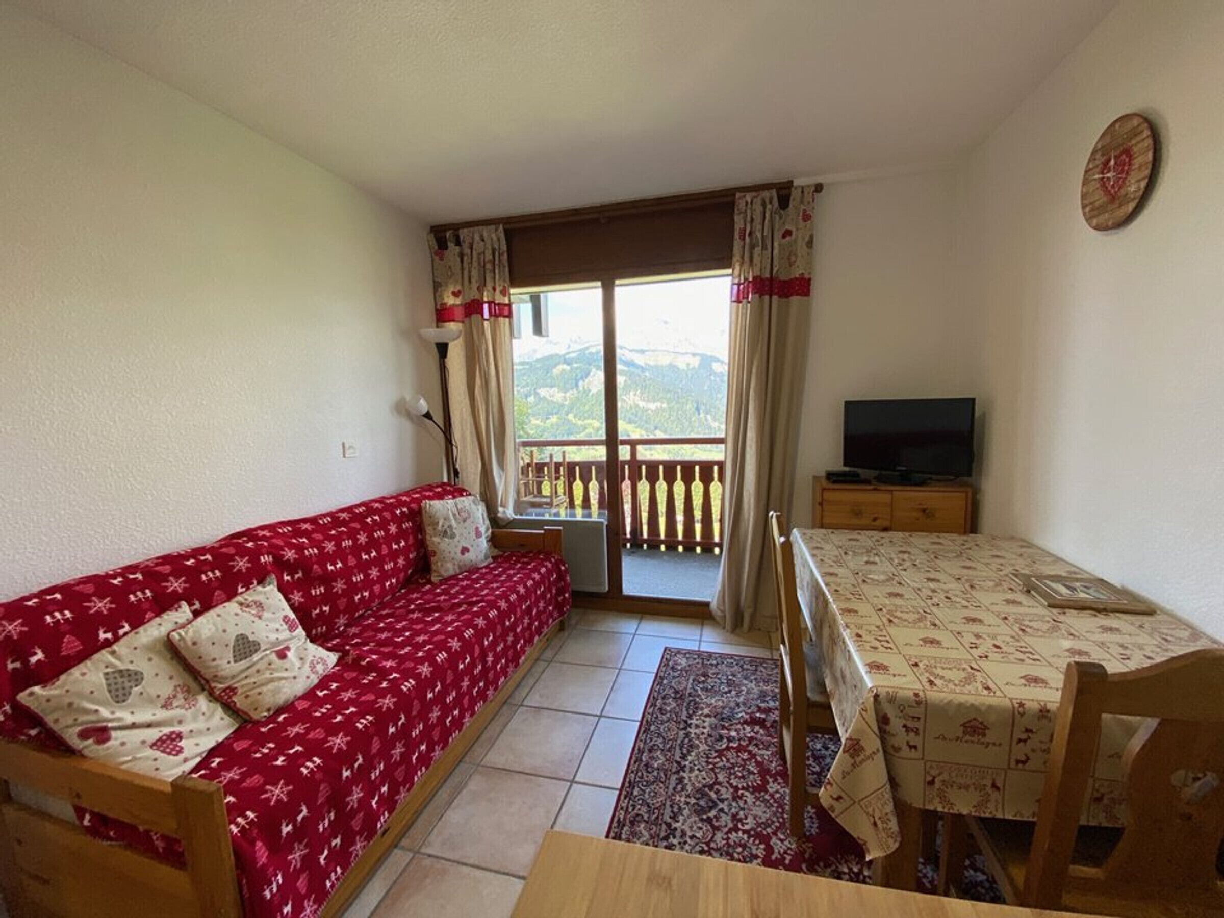 A cozy room with a red sofa, a wooden dining table, and a TV.