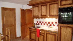 A kitchen with wooden cabinets, a tiled backsplash, and a black stove. - Cozy Apartment for 6 with Pool, Balcony, and Private Parking in Crest-Voland (Crest-Voland)
