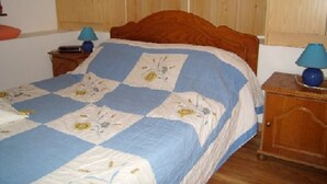 A bedroom with a wooden bed frame, a blue and white quilt, two bedside tables with lamps, and wooden cabinets. - Cozy Studio-Mezzanine for 4 with Balcony, Near Slopes & Village – Pet Friendly (Crest-Voland)