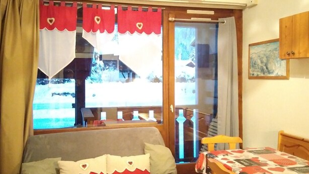 A cozy room with a bed, a table, and a view through a glass door. - Cozy Studio-Mezzanine for 4 with Balcony, Near Slopes & Village – Pet Friendly (Crest-Voland)