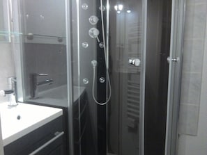 A modern bathroom with a glass-enclosed shower, a white sink, and a towel rack.