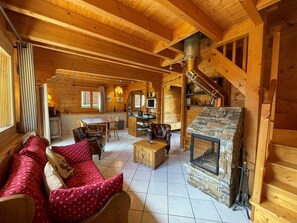 Accogliente interno di una baita di legno con un caminetto in pietra, arredi in legno e un'area pranzo.