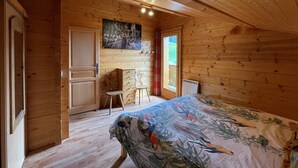 Ein Schlafzimmer in einer Holzhütte mit einem Bett, einem Schminktisch, einem Stuhl und einem Bild an der Wand.