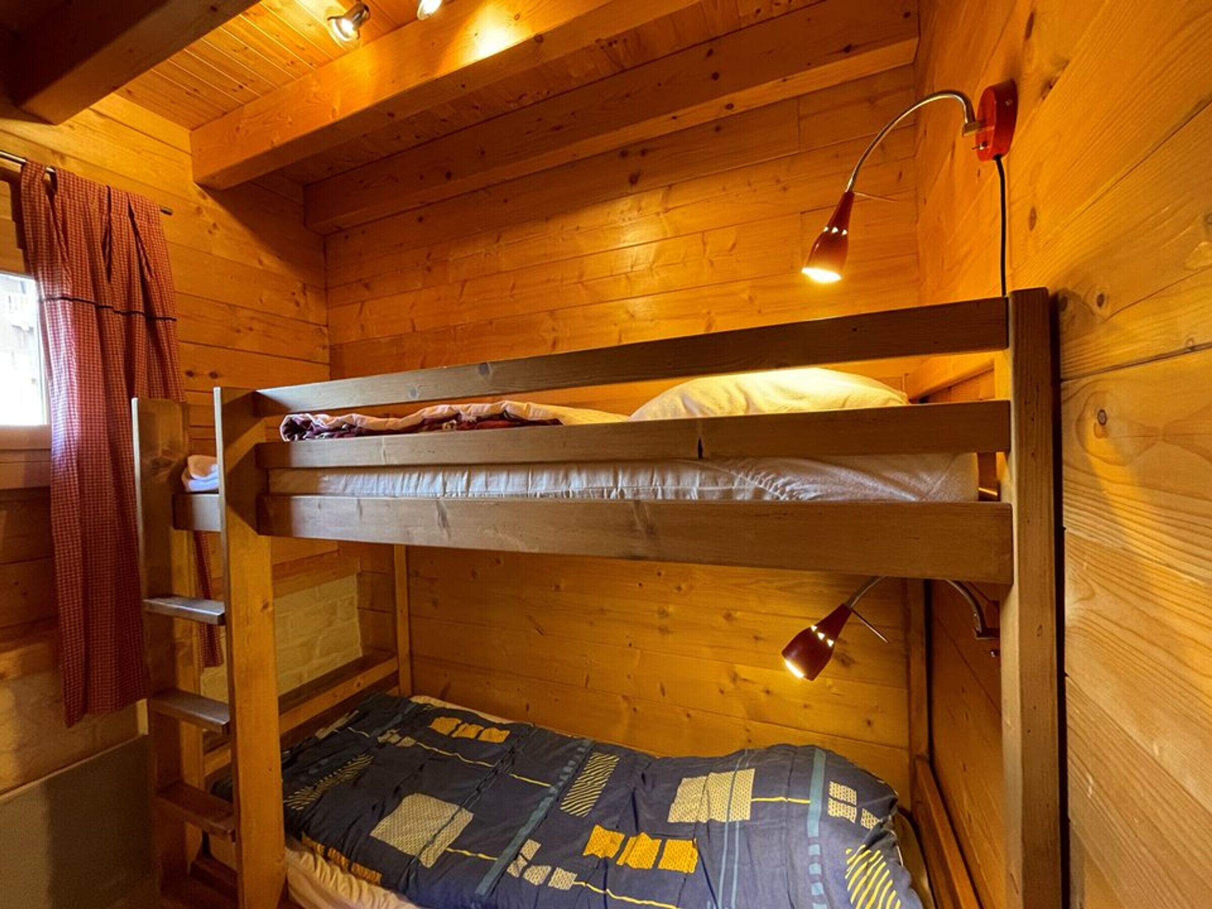 A bunk bed room with wooden walls, a ladder, and two bedside lamps.